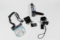 Three digital cameras with carrying cases and accessories including a waterproof camera bag and a mini tripod on white background.