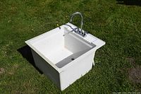 Full view of white utility sink on grass showing sink basin and faucet