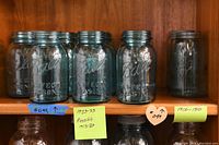Four blue glass vintage Ball Mason jars on wooden shelf with metal lids and dated sticky notes