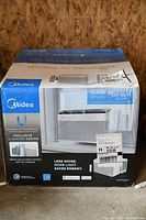 Front view of boxed Midea window air conditioner showing brand logo, U-shaped design and BTU rating