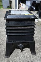 Side view of black worm composting bin with five stacked trays and black spigot plus stand.