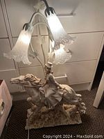 Full view of the Angelica Collection lamp showing the statue base of a woman riding a horse and the three flower-shaped glass light shades illuminated.