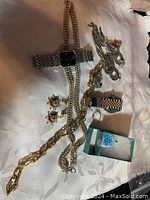 Photo showing chain necklaces, large dangling earrings, smaller stud earrings, and metal wristwatches on tablecloth