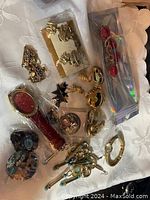 Assorted vintage jewelry on white fabric, including bracelets, earrings, brooches, and pins in mixed metals and colorful accents.