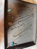Grey tray set with various vintage fashion necklaces arranged flat, displaying chains and pendants clearly.