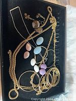 Overview of assorted jewelry in a black display tray including gold-tone chains, cabochon earrings, and gold-tone bangles