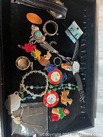 Assortment of jewelry including pins, rings, necklaces, watches, and small decorative charms laid out in a black jewelry tray.
