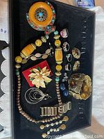 Top down view of assorted jewelry in black tray showing necklaces, rings, brooch, bracelets, and earrings