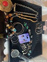 Wide view of assorted jewelry items displayed on a black velvet surface, including necklaces, bracelets, earrings, rings, and a wristwatch.