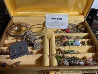 Top view of the open Lady Buxton jewelry box showing various costume jewelry rings, bracelets, and brooches organized in the ring slots and compartments.