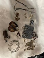 Top view of assorted earrings, necklaces, charms spread on fabric, showing variety of shapes and styles