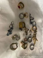 Top-down view showing all items in the lot on white fabric, including rings, earrings, charms, and pendants.