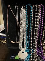 Photo showing assorted necklaces hanging, including bead strand necklaces in various colors and metal chains with pendants on a black background