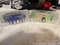 Photo showing two pairs of Pit Viper polarized sunglasses in clear plastic boxes, one pair with blue frames, one with lighter iridescent lenses.