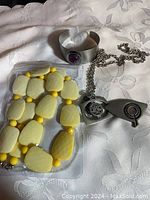 Lot including the silver-tone cuff bracelet with amethyst stone, stainless steel compass pendant necklace, and yellow beaded necklace.