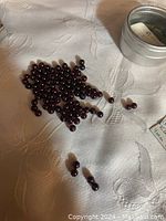 Multiple round garnet gemstones placed on a white fabric background next to a small metal container.