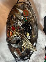 Top-down view of oval silver plated tray filled with assorted vintage fashion jewelry including bead necklaces, pins, chains, rings, and bangles.