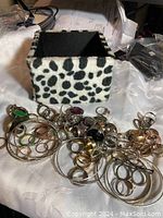 Photo showing tiger print box open with assorted rings and bangles spread around it on a white cloth.