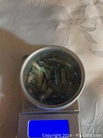 Top view of turquoise tube-shaped gemstones placed in a small round container on a digital scale showing weight.