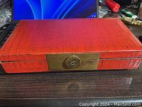 Exterior front view of rectangular red vintage box with brass lock on a dark surface.