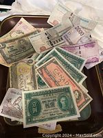 Photo showing vintage Coca Cola tray holding assorted vintage world currency notes with various denominations and countries of origin.