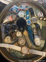 Oval Coca Cola tray holding assortment of vintage watches and pins, ceramic honeybadger decanter, and other small items.