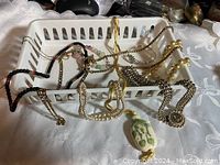 Photo showing several pieces of vintage fashion jewelry including necklaces and bracelets in a white plastic basket on a lace tablecloth.