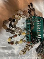Photo of vintage fashion jewelry pieces including bracelets, necklaces and green basket container, showing multiple items in used condition.