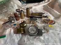 Wide view of all items showing lighters, brass containers, wooden figurine, pins in bags, and a pressure gauge.