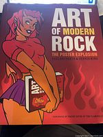 Front cover of 'Art of Modern Rock: The Poster Explosion' book showing illustration of a cartoon woman in red with flame graphics and title text.
