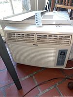 Front view of Haier window air conditioner with white housing, front air vents, and remote control placed on top.