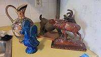 Photo showing Mexican pottery ewer, blue rooster figurine, carved wood goat, caribou and moose figures.