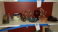 Shelf displaying the lot including ceramic pitcher, pottery bowls, amber glass goblet, and Goebel figure.