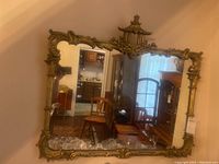 Full view of the wall mirror showing its rectangular shape with ornate brass tone Asian pagoda inspired frame, placed on a wall reflecting part of a living room.