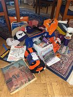 Photo showing an assortment of Baltimore sports gear including caps, seat cushions, scarf or throw, magazines, and cups arranged on a floor with a carpet.