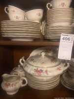 Front view inside cabinet showing stacks of plates, cups, covered serving dish, sugar bowl, and creamer with floral designs and gold accents.