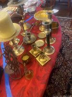 Wide view of the lot on red tablecloth showing brass candlesticks, figurines, candle snuffer, bell, and footed bowl.