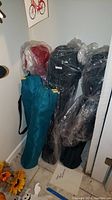 Five folding chairs stored upright against a wall, some wrapped in plastic. Items include three camp chairs and two in green bags.