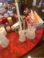 Photo of candles on a red tablecloth including jar candles, pillar candles, votive candles, and glass candlesticks with white tapered candles.