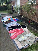 Clothing items laid out on blankets outside showing multiple tops, pants, and shorts in various colors and styles.