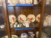 Shelf of Christmas Cardinal plates and various ceramic decorative and tableware items including small vases, bowls and pitchers.