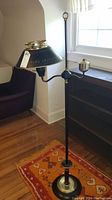 Enamelware tole floor lamp shown standing on a patterned rug next to bookcase and chair