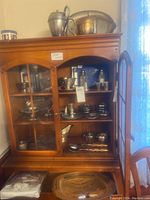 Cabinet with multiple shelves containing silverplate serving items including pitchers, trays, bowls, cups, plates, and coasters.
