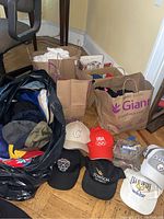 Overview photo showing six ball caps on the floor in front of three brown branded grocery bags filled with socks and other apparel items.