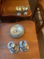 Photo showing pair of weighted sterling silver candle holders, oyster shell shaped dish with salt and pepper shakers, and creamer and sugar set on wooden tables.