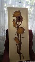 Tall narrow framed textile embroidery of sunflower design with detailed stitching in brown, orange and yellow hues on beige fabric
