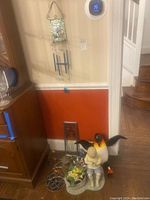 Wide angle photo showing ceramic garden figures, penguin figure, metal artisan garden sculpture, and stained glass inspired wall art hanging above.