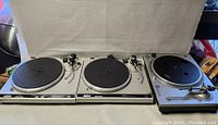 Front view of three turntables side by side: two Technics models and one Stanton unit