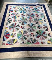 Full view of the hand-made quilt laid out flat showing the full Dresden Plate pattern with multi-colored fabric wedges in varying sizes on cream ground and blue and cream borders.