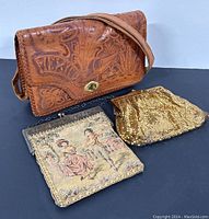 Three ladies purses displayed together: a tooled leather purse, a gold-tone metal mesh purse, and a tapestry coin purse with vintage embroidery.
